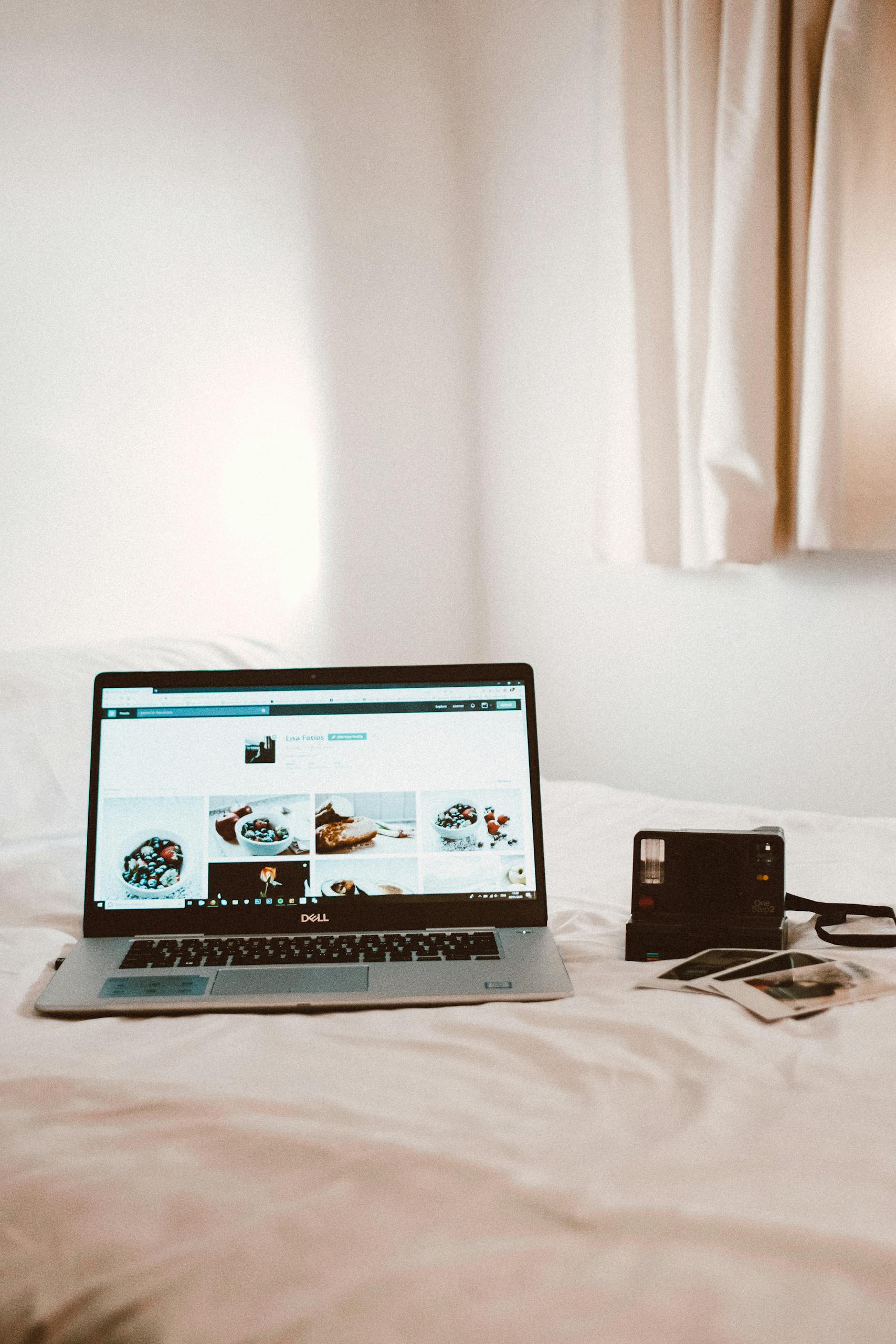 Cozy bedroom with a laptop and vintage camera on a white bed.